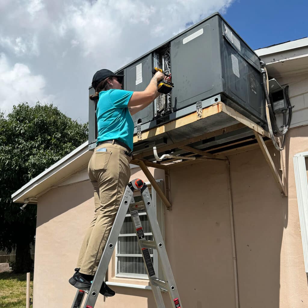 a woman on a ladder working on a air conditioner